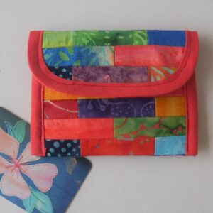 Envelope style coin purse made from a patchwork of multi-coloured batik fabrics and trimmed in orange.