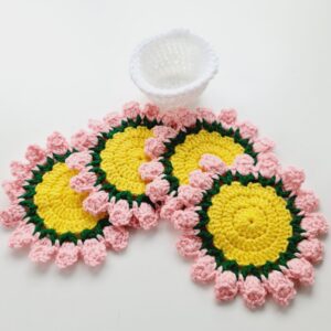 Crochet flower coasters set with white storage pot. Yellow middle, green stems and pale pink clusters.