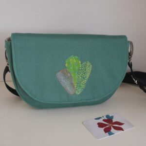 Green fabric bag with detachable strap and collection of three cacti appliqued onto the front flap