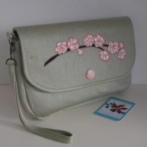 Pale apple green clutch bag with detachable wrist strap and spray of cherry blossom appliqued onto the flap of the bag.