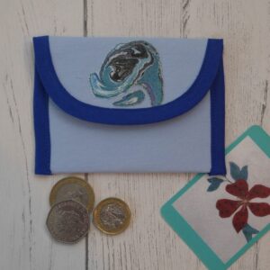 Light blue fabric coin purse with royal blue trim and abstract appliqued design on the flap. Shown flat and closed with a selection of coins and business card.