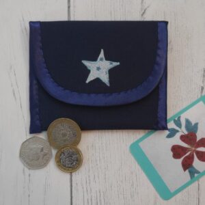 Navy envelope style coin purse made from fabric with an appliqued star on the flap, shown with a selection of coins and a business card.