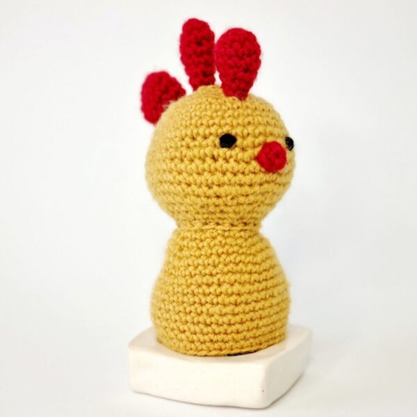 Yellow and red crochet chicken sat on top of a white egg cup
