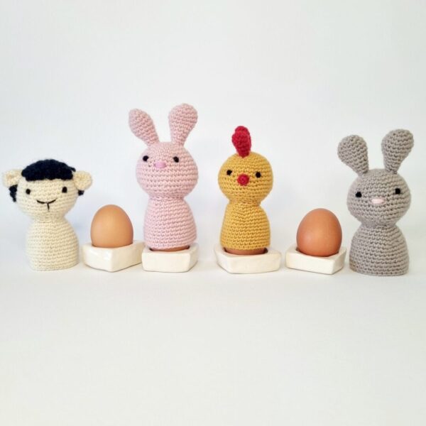 4 crochet farm animal egg cosies sat with white egg cups and eggs