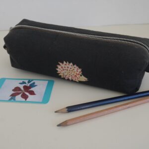 Black box style pencil case with appliqued hedgehog shown with two pencils.