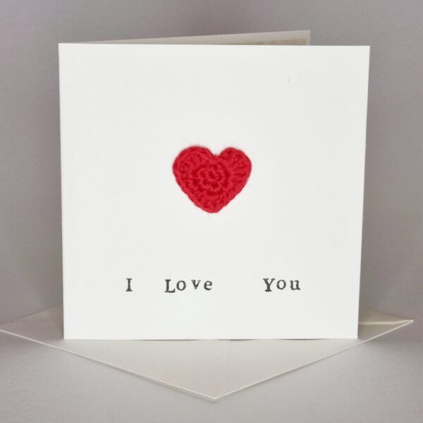 A simple cream card with the words 'I love you' written on the front and a red love heart. It's sat on top of a cream envelope. All on a white grey background