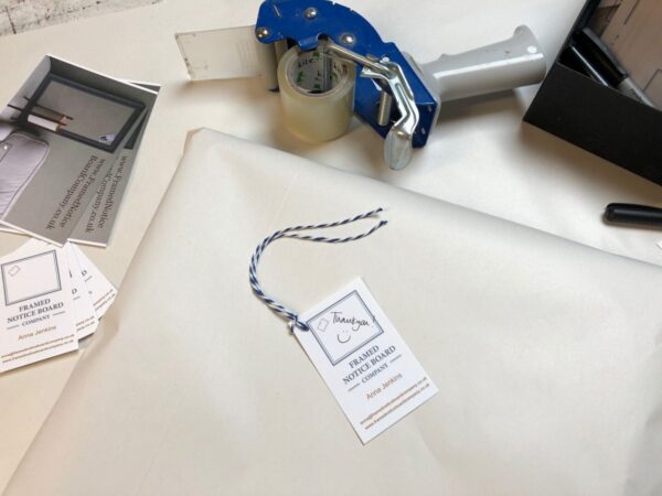 Picture of packing process with postcards, business cards, tape dispenser and recycled white wrapping and packing paper.