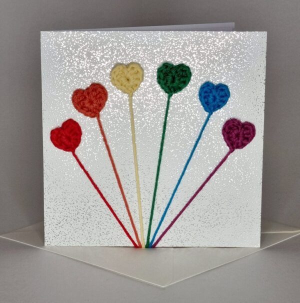 Rainbow coloured crochet hearts on a silver sparkly square greetings card, sat on top of envelope