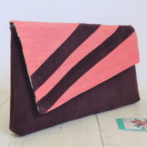 A clutch bag with an asymmetric flap made from two contrasting fabrics: plum soft feel polyester for the body of the bag and two slanting stripes on the flap, textured peach coloured cotton for the rest of the flap.