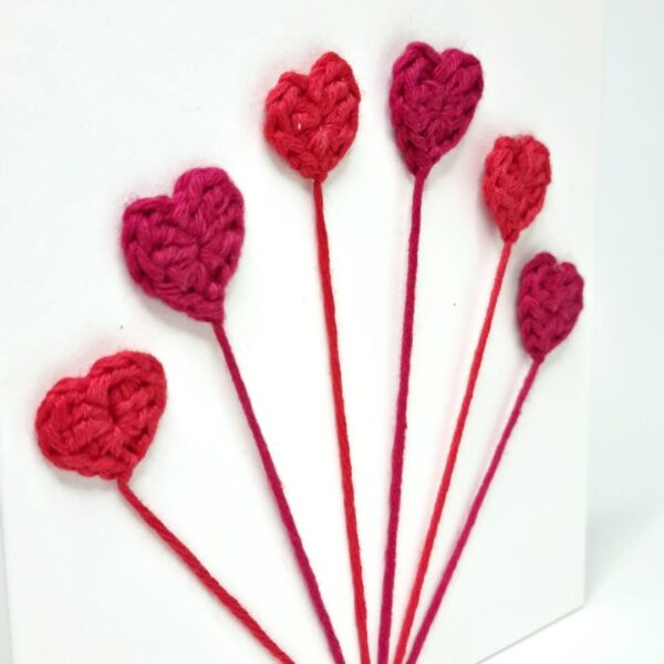 A close up shot of 6 crochet hearts on a thread on a white background.