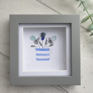 Seaglass flowers in a blue and white cornishware inspired jug. Framed in a grey box frame.