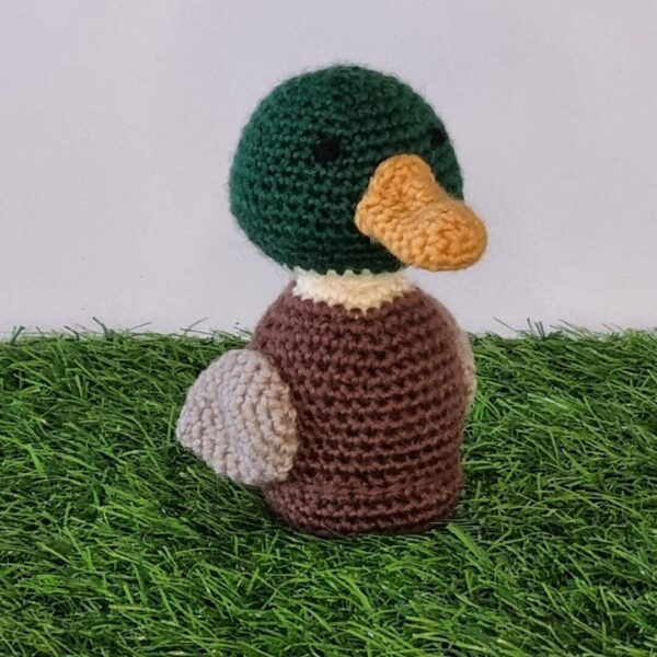 Crochet mallard duck sat on green grass with white background