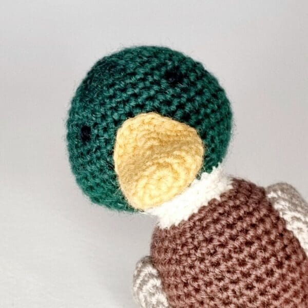 A close up of a crochet mallard duck head on white background