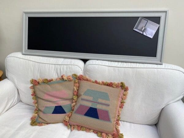 A long magnetic blackboard with ornate frame painted a pale grey.