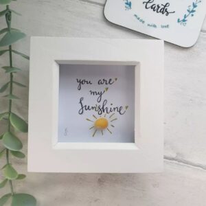 Handmade shell sunshine picture, made with a yellow periwinkle shell with the song lyric - You are my Sunshine.