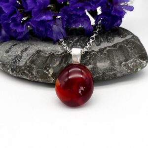 small glass cabochon in shades of red mounted in silver on a silver chain