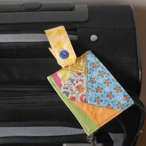 The top of a suitcase with a brightly coloured patchwork luggage tag attached to its handle