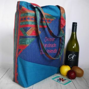 Front and side view of tote bag with triangular patches in blue, red and green fabrics, shown with bottle of wine and 3 items of fruit.