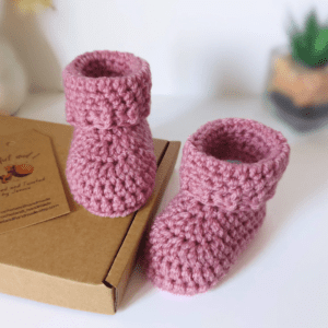 A pair of pink newborn baby booties which are made and ready to be posted. The are made in one piece from the sole up, and they are finished with a cute little folded cuff.