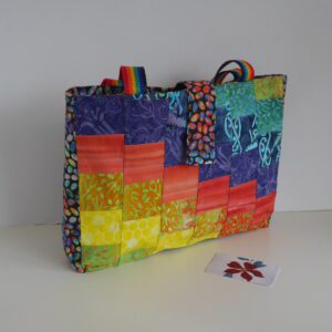 Tote bag made from patchwork of bright rainbow coloured batik fabrics, and rainbow striped webbing handles.