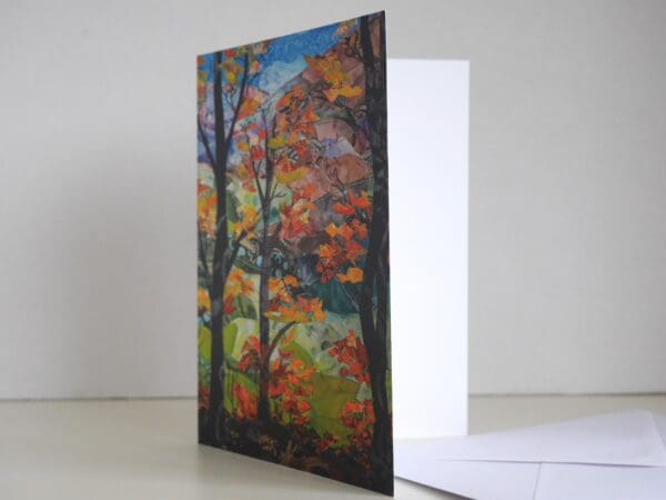 Greetings card standing up and open to show blank inner, picture on front of woodland with autumnal foliage and distant hills in background.