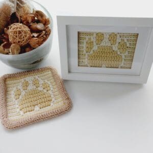 Paw print picture and mat made by Sarah Lou Crafts, in gold and cream to represent a golden retriever dog. Shown in a white box frame with unframed mat laying next to it both on a white table.