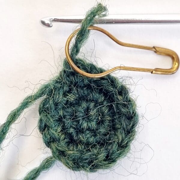 a crochet circle in bottle green with a gold stitch marker and a silver tip of a crochet hook