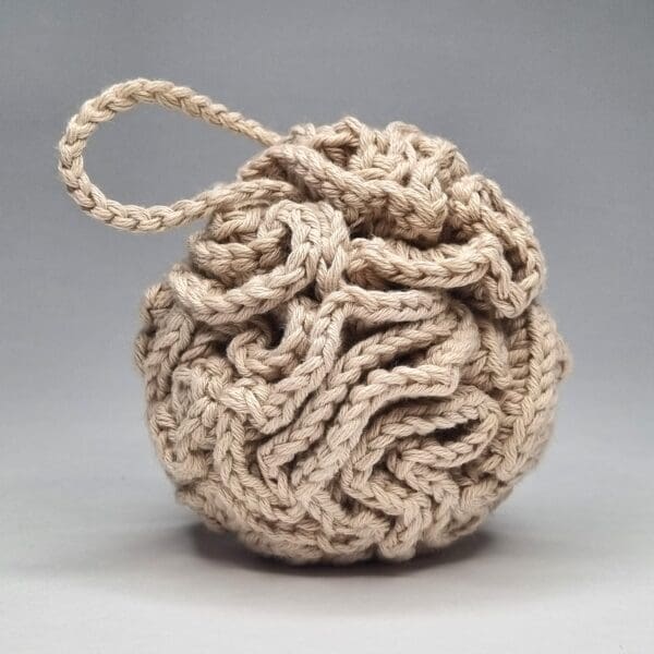 A beige shower puff made with organic cotton yarn on a white background