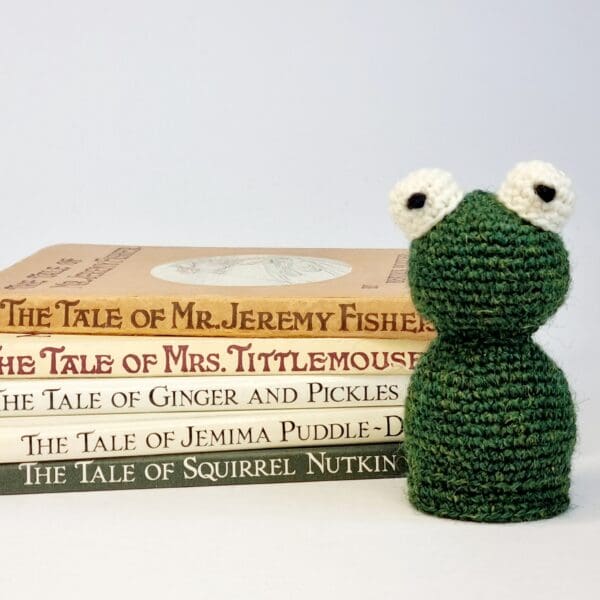 Crochet bottle green frog sat next to some children's books