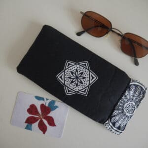 Black rectangular glasses case with black and white geometric design appliqued onto centre and black and white printed trim around the opening. Shown with sunglasses.