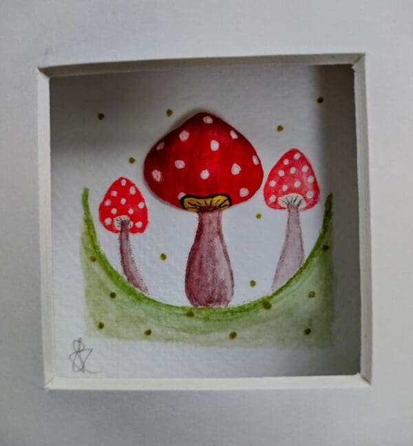 Three red and white toadstools hand painted in water colour paints, one of which is made up of a hand painted clam shell. Framed in a black box frame with mount.