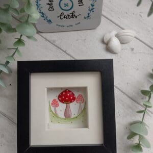 Three red and white toadstools hand painted in water colour paints, one of which is made up of a hand painted clam shell. Framed in a black box frame with mount.