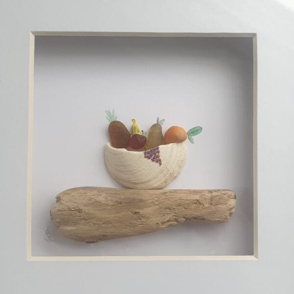 Mounted and framed picture of a bowl of fruit using genuine beach treasure of driftwood, seaglass, shell and broken clam shell.