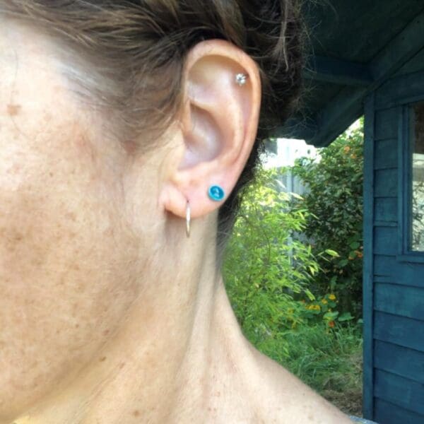 1cm and 2cm Silver Hammered Mini Hoop Earrings handmade from recycled silver. Complete round hoops. Side view of me wearing the 1cm hoops with mini silver and turquoise enamel stud earring