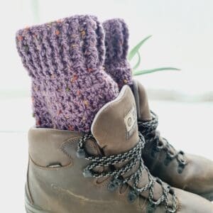 Purple amethyst crochet boot cuffs made by Sarah Lou Crafts, shown in brown Scarpa Hiking Boots on a white table with green aloe vera plant in the back ground.