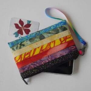 Zipped pouch made from strips of batik fabrics in a selection of bright colours, shown with phone partly in the case.