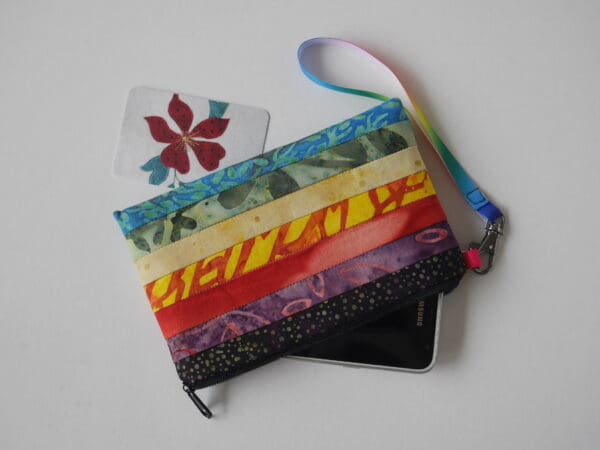 Zipped pouch made from strips of batik fabrics in a selection of bright colours, shown with phone partly in the case.