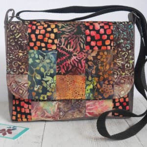 Front view of messenger style bag made from patchwork fabrics in autumnal colours with brown sides and strap.