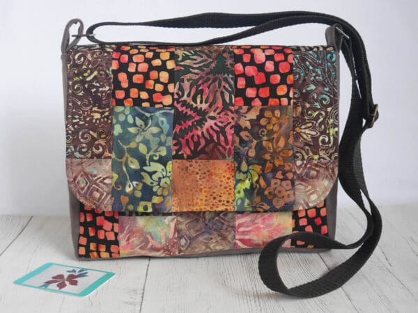 Front view of messenger style bag made from patchwork fabrics in autumnal colours with brown sides and strap.