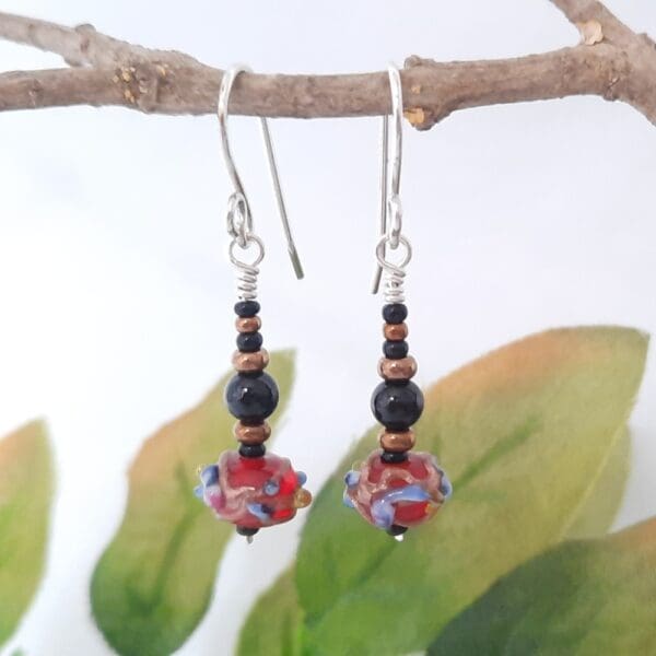 Black and bronze beaded drop earrings with a red Venetian bead at their base and fitted with sterling silver ear hooks.