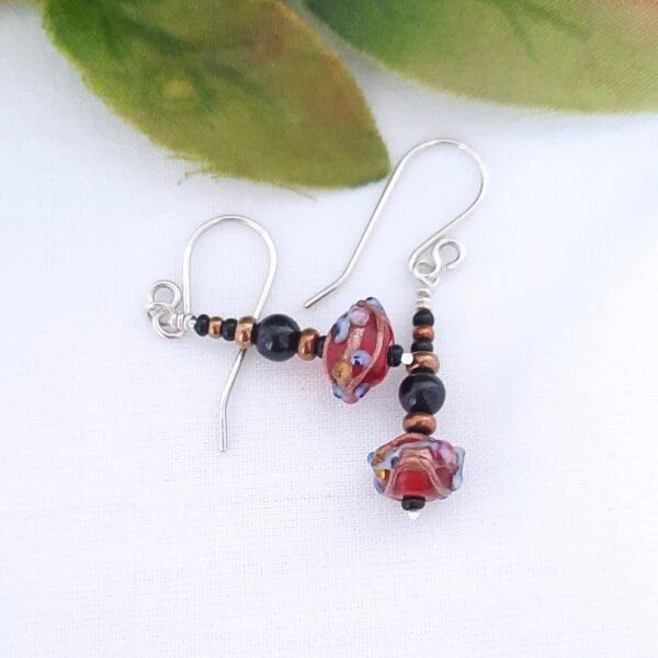 Black and bronze beaded drop earrings with a red Venetian bead at their base and fitted with sterling silver ear hooks.