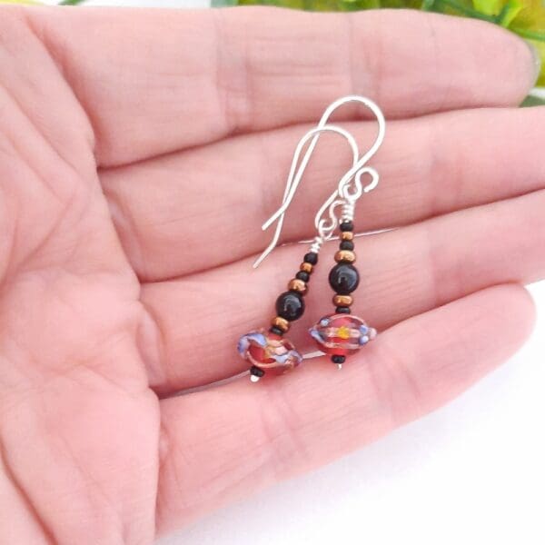 Black and bronze beaded drop earrings with a red Venetian bead at their base and fitted with sterling silver ear hooks.