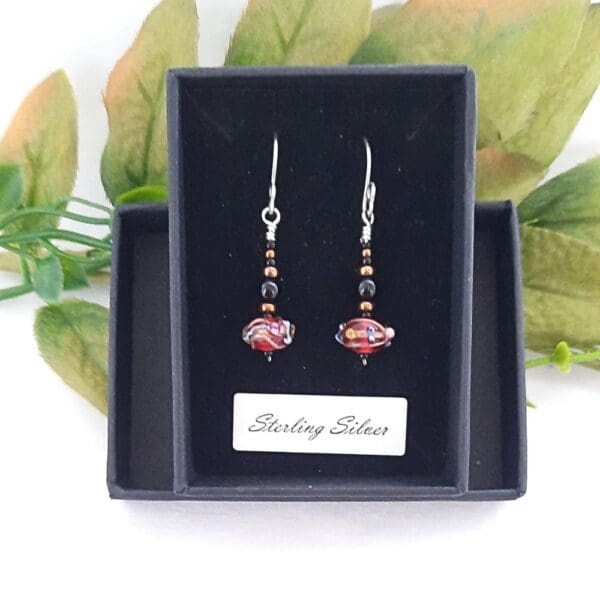 Black and bronze beaded drop earrings with a red Venetian bead at their base and fitted with sterling silver ear hooks.