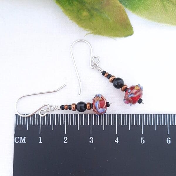 Black and bronze beaded drop earrings with a red Venetian bead at their base and fitted with sterling silver ear hooks.