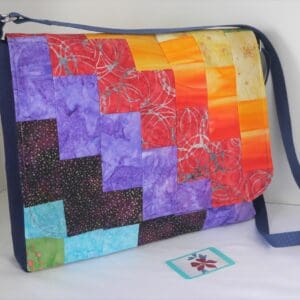 This is a large messenger style satchel made from a patchwork on rainbow coloured fabrics positioned to give diagonal bands of colour.