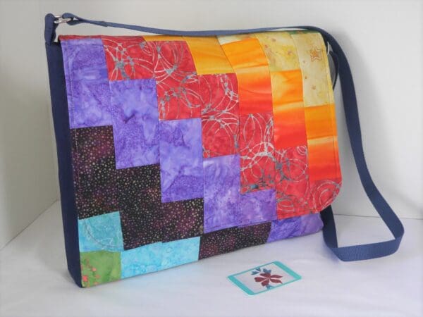 This is a large messenger style satchel made from a patchwork on rainbow coloured fabrics positioned to give diagonal bands of colour.