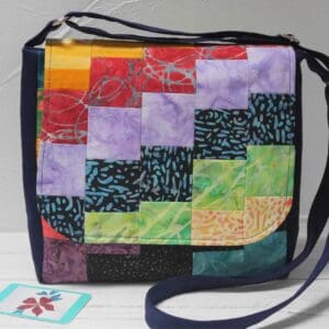 Front view of crossbody bag made from patchwork squares in rainbow colours, arranged diagonally.