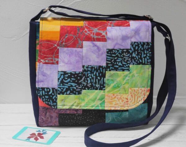 Front view of crossbody bag made from patchwork squares in rainbow colours, arranged diagonally.