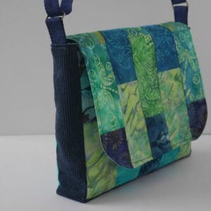 Side view of messenger style bag showing navy side panels and patchwork flap in shades of blue and green.