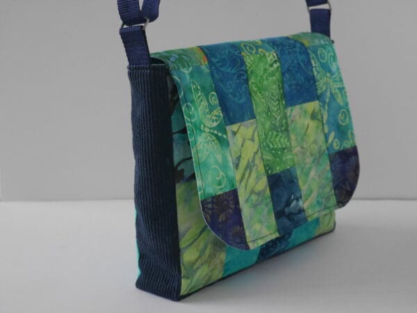 Side view of messenger style bag showing navy side panels and patchwork flap in shades of blue and green.